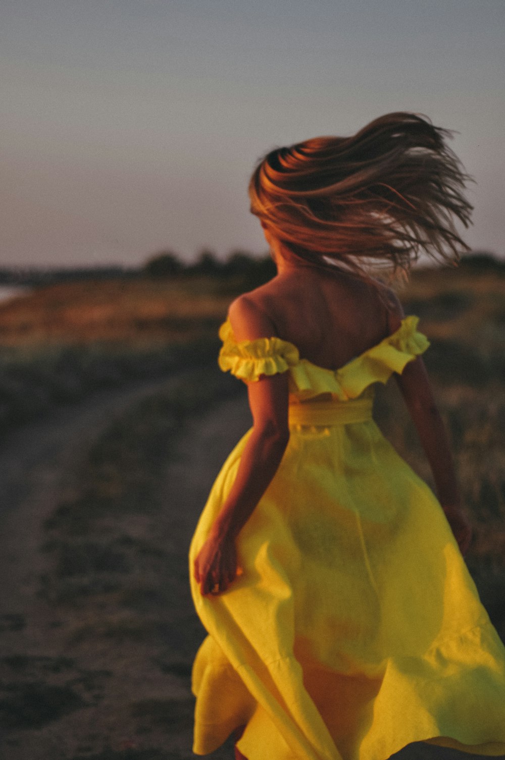 a woman in a yellow dress walking down a dirt road