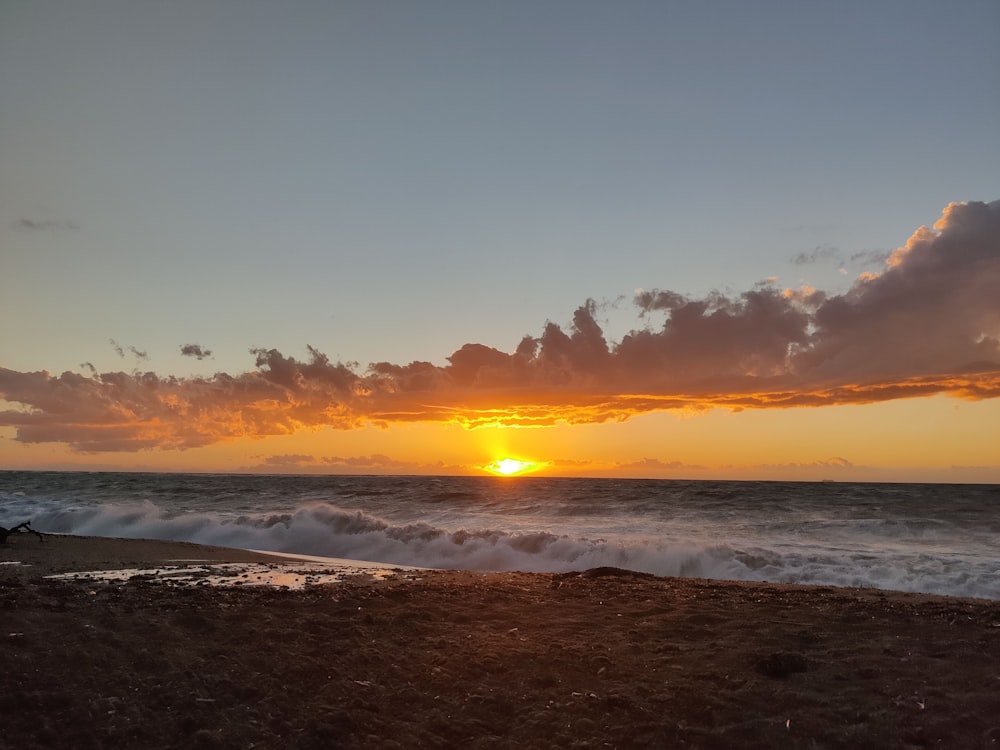 the sun is setting over the ocean on a beach