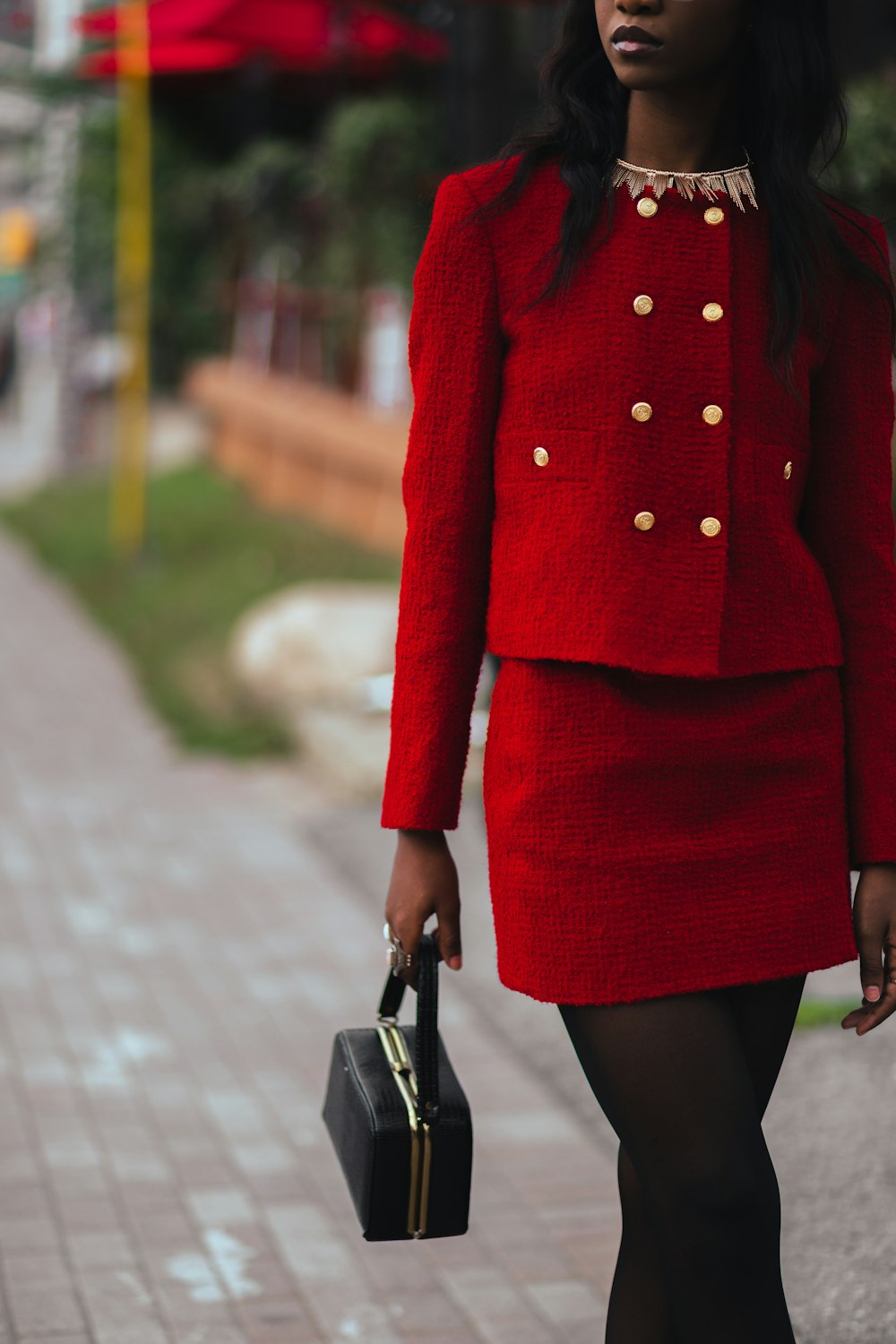 a woman in a red jacket and skirt walking down the street