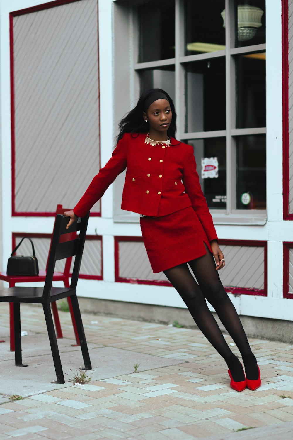 a woman in a red suit leaning on a chair