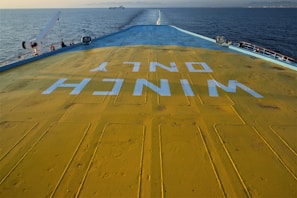 The image captures the deck of a ship with a large, visible yellow surface marked with blue text that reads 'WINCH ONLY' in reverse. The ocean is visible on both sides, and a distant ship can be seen on the horizon.
