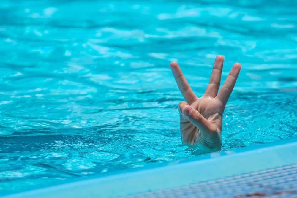 uma pessoa fazendo um sinal de paz em uma piscina