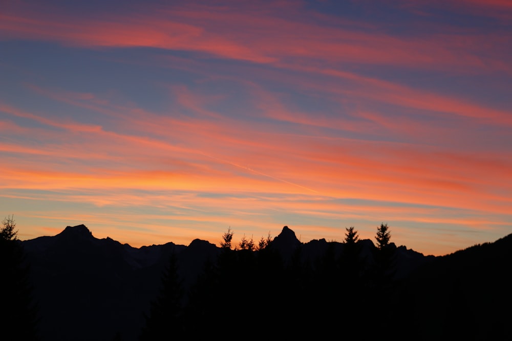 a sunset view of a mountain range with trees in the foreground