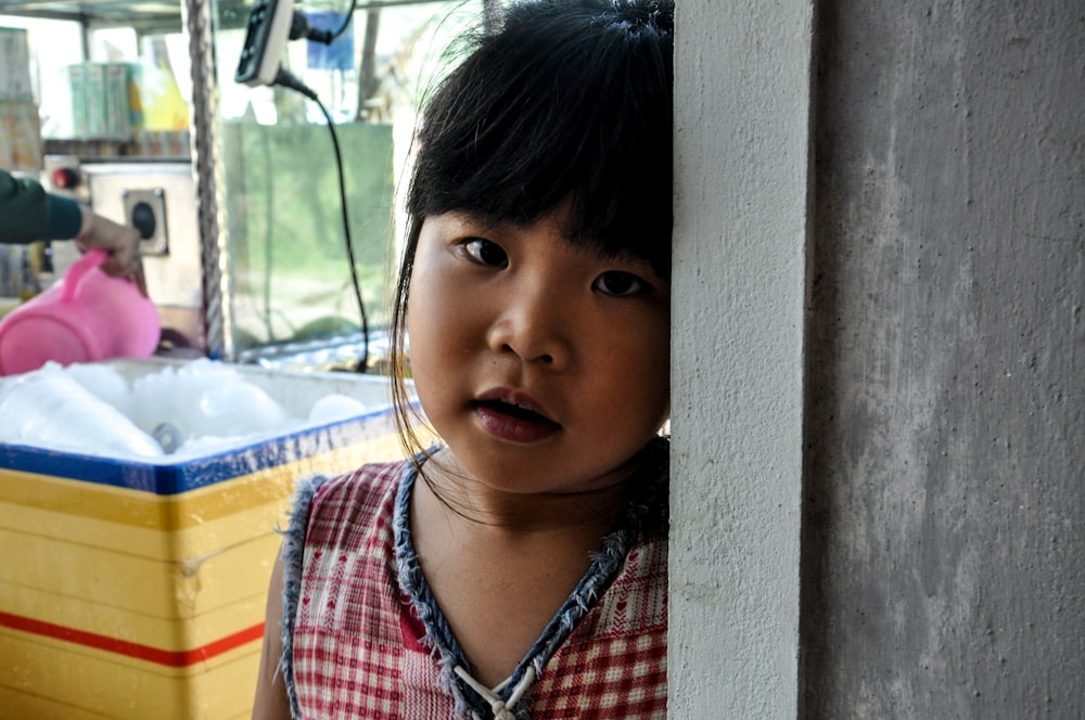 a little girl peeking out from behind a wall