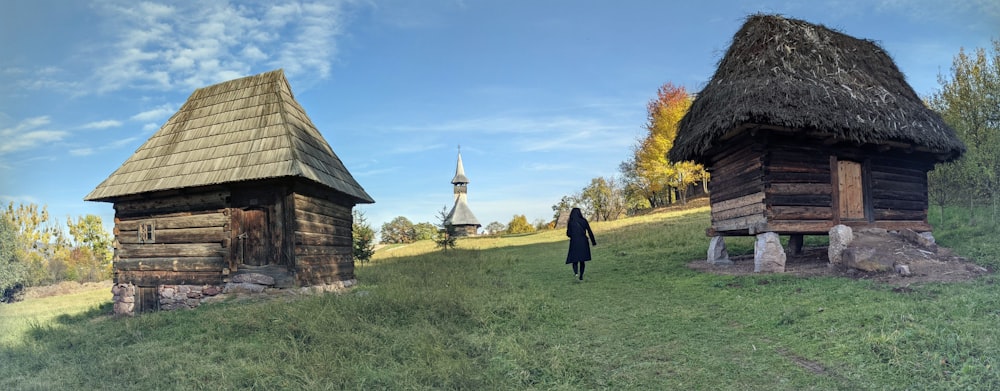 a person standing in a field next to two wooden buildings