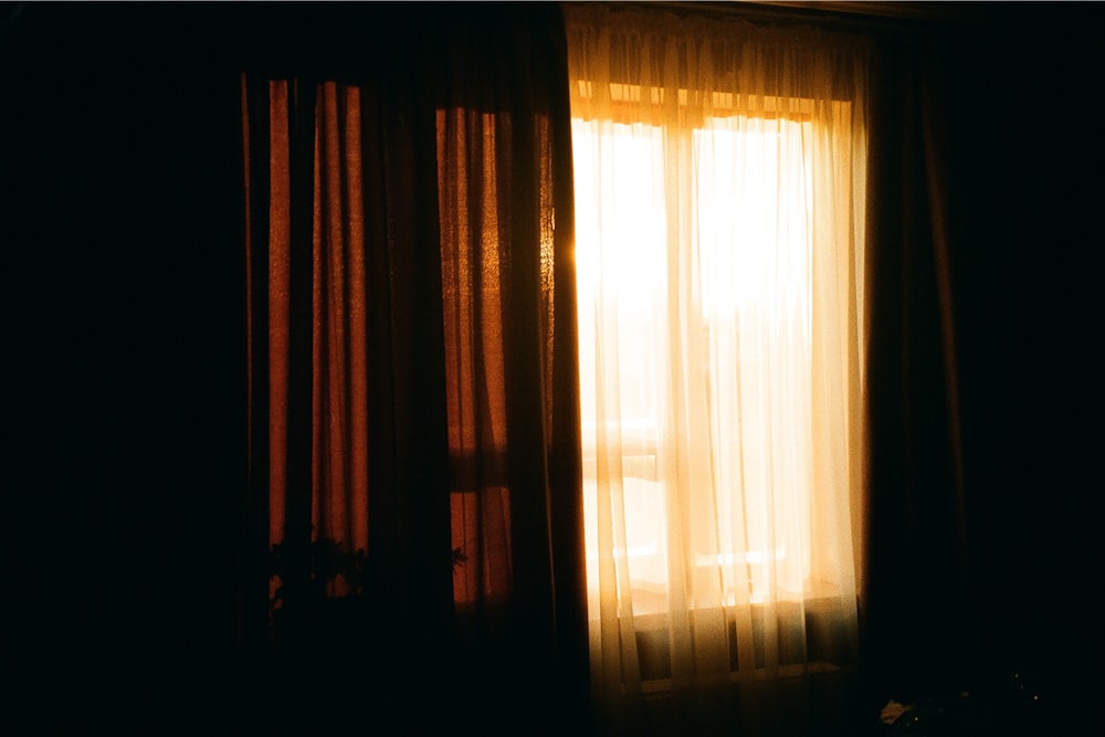 une chambre sombre avec une fenêtre et un rideau