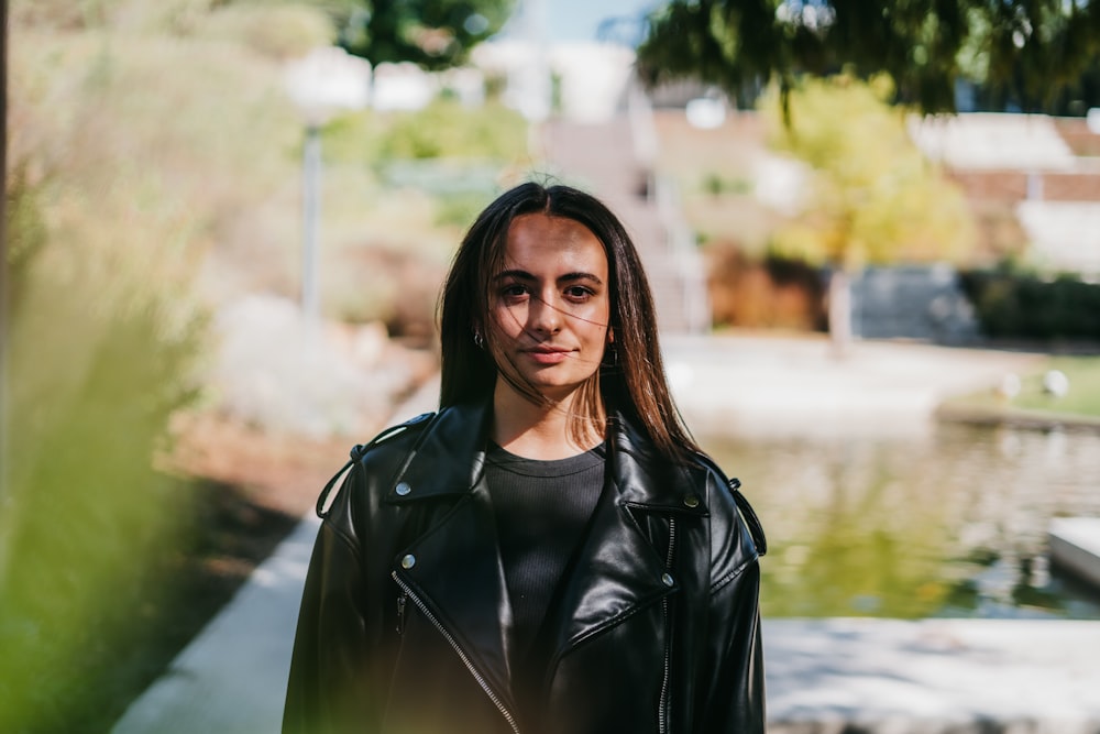 a woman in a black leather jacket standing in front of a pond