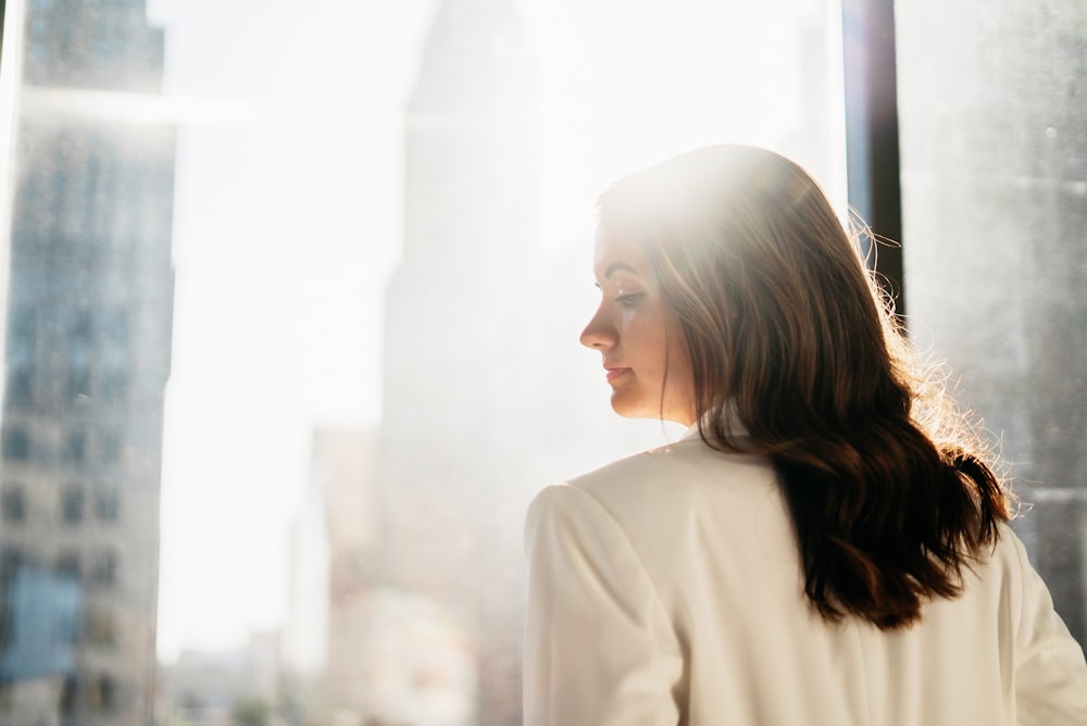 a woman standing in front of a window looking out at the city