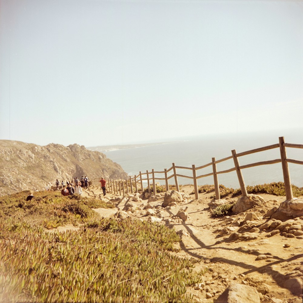 um grupo de pessoas subindo uma colina ao lado de uma cerca de madeira