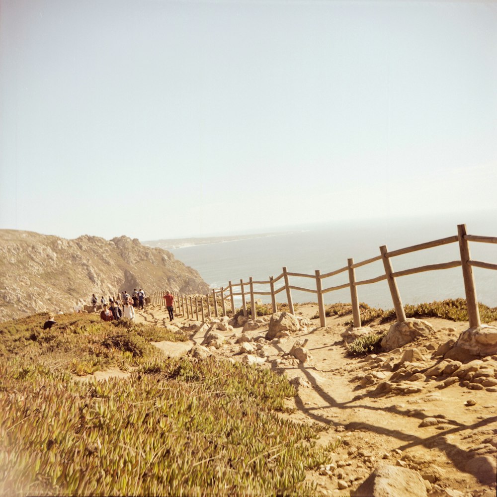 a group of people walking up a hill next to a wooden fence