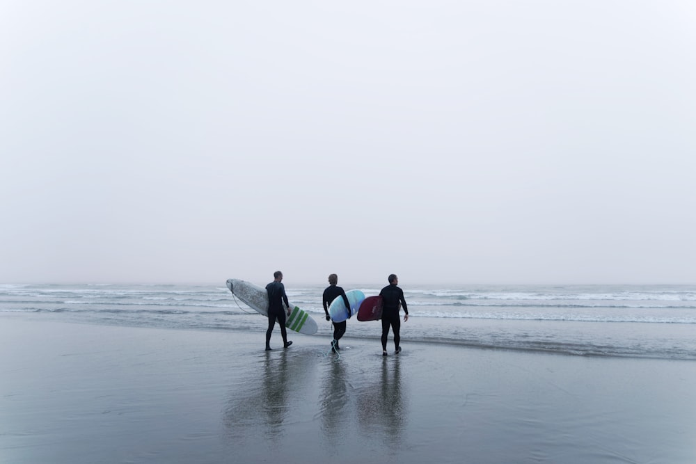 three surfers walking on the beach with their surfboards