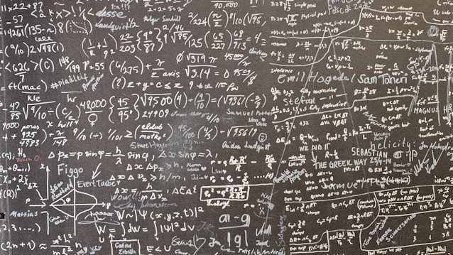 A large blackboard filled with complex mathematical equations, symbols, and annotations written in chalk. The writing is dense and covers the entire surface, indicating a thorough and detailed exploration of mathematical concepts. Various mathematical operations, symbols like integral, summation, and square roots, are visible along with arrows and diagrams.