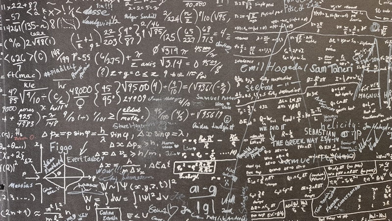 A large blackboard filled with complex mathematical equations, symbols, and annotations written in chalk. The writing is dense and covers the entire surface, indicating a thorough and detailed exploration of mathematical concepts. Various mathematical operations, symbols like integral, summation, and square roots, are visible along with arrows and diagrams.