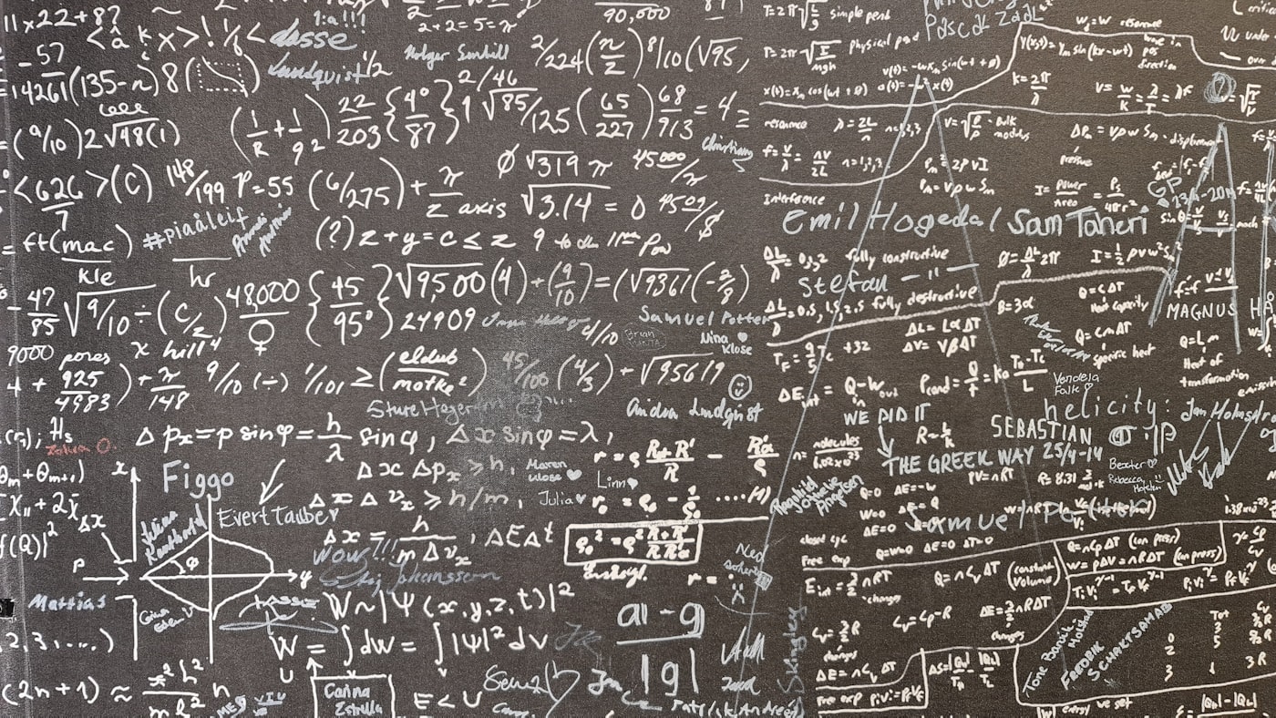 A whiteboard densely covered in handwritten mathematical equations and geometric diagrams sits beside a laptop.