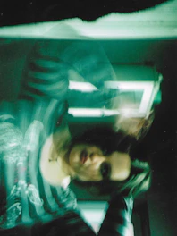 A blurry photo of a shadowy figure in a green and blue tinted setting.