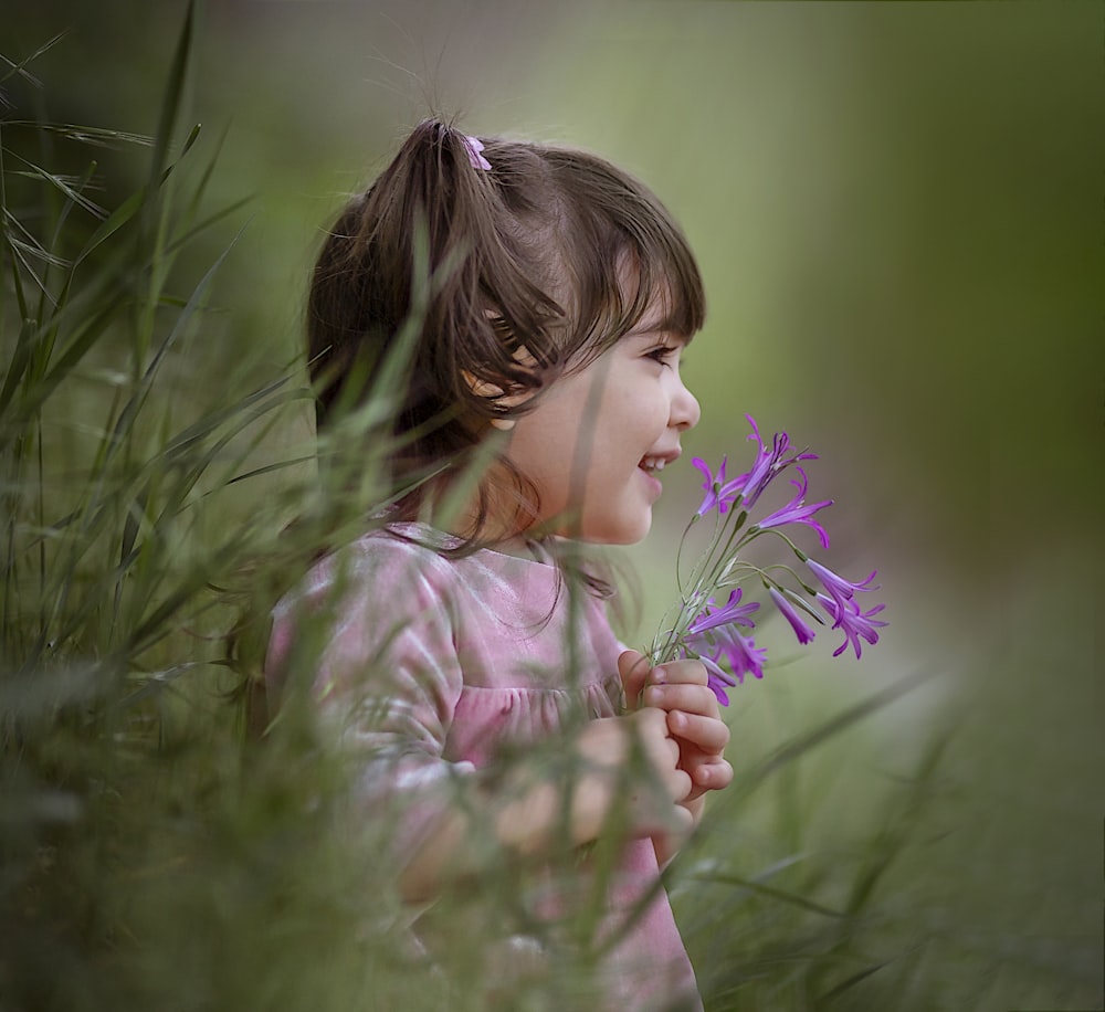 a little girl holding a purple flower in her hands