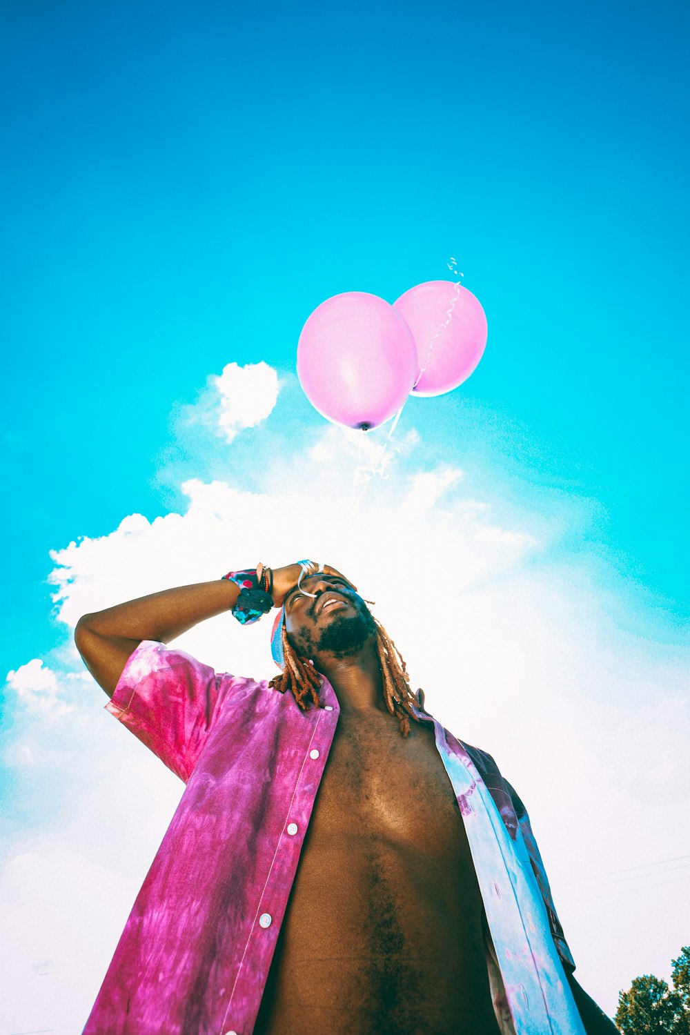 a man with a pink shirt and two balloons in the sky