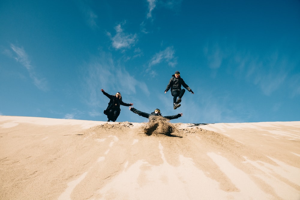 three people jumping in the air on a sand dune