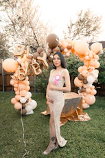 a pregnant woman standing in front of a balloon arch
