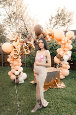 a pregnant woman standing in front of a balloon arch