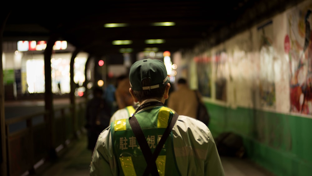 a man in a green vest and hat walking down a hallway