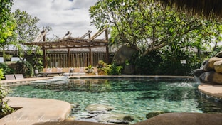 a pool surrounded by rocks and trees with a gazebo in the background