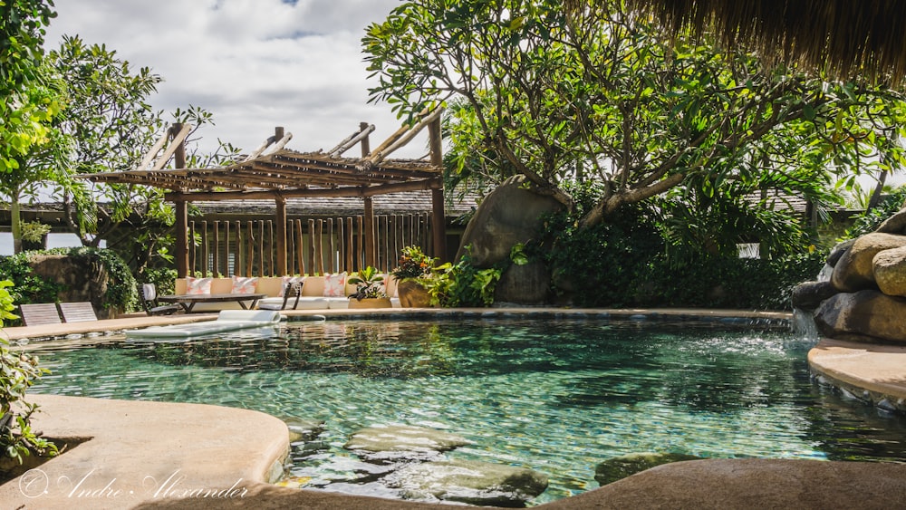 a pool surrounded by rocks and trees with a gazebo in the background