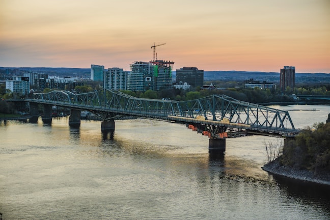 A sleek steel bridge under construction with workers inspecting beams at sunset.