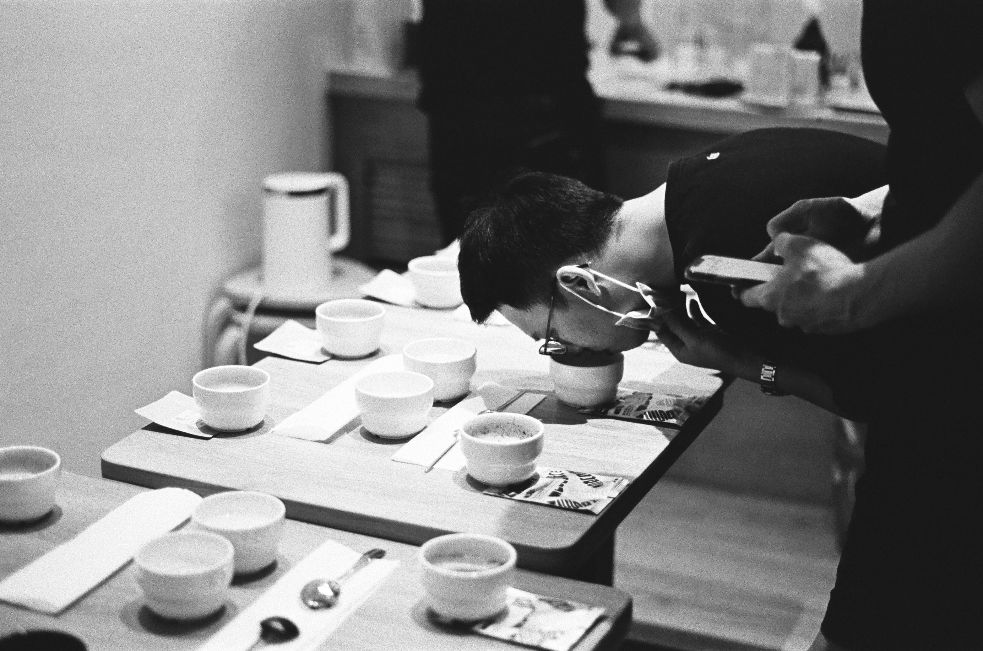 Group of coffee enthusiasts gathered around a cupping table smelling and tasting different coffees