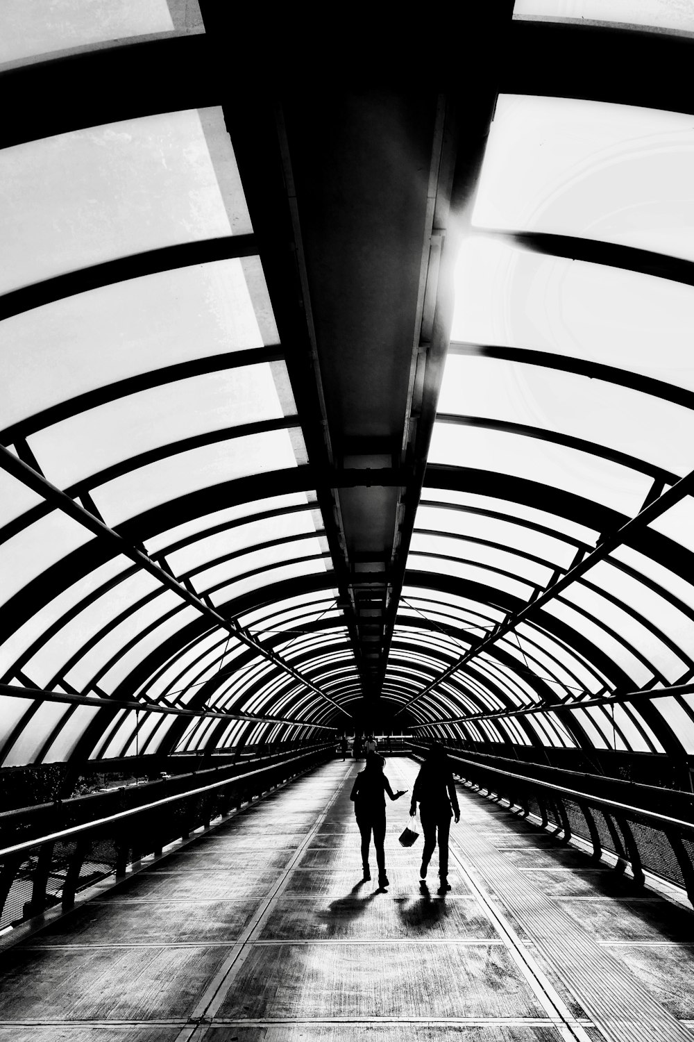 a black and white photo of two people walking down a walkway