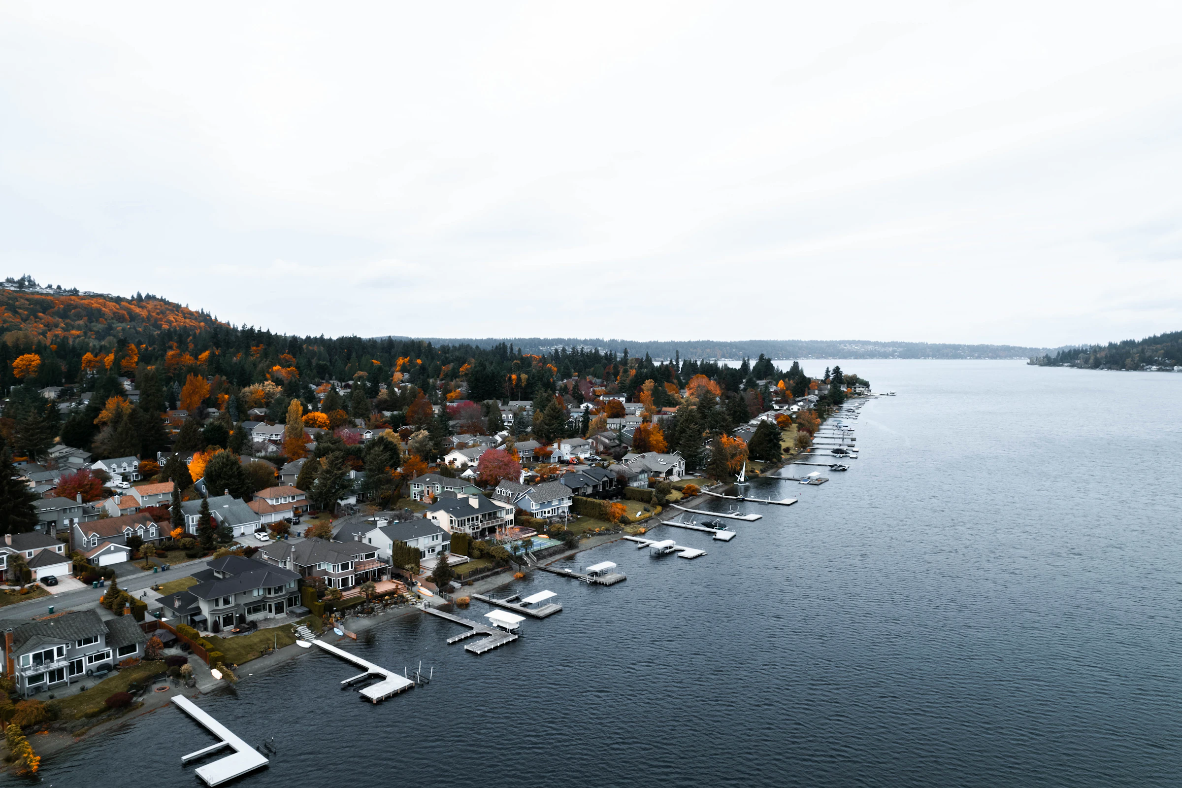 Aerial view of lakefront homes with private docks along a calm shoreline, autumn trees behind