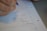 A close-up of a hand holding a pen, writing mathematical calculations on a sheet of graph paper. The paper is blue and white, filled with numbers in a column format, possibly performing division or multiplication tasks.