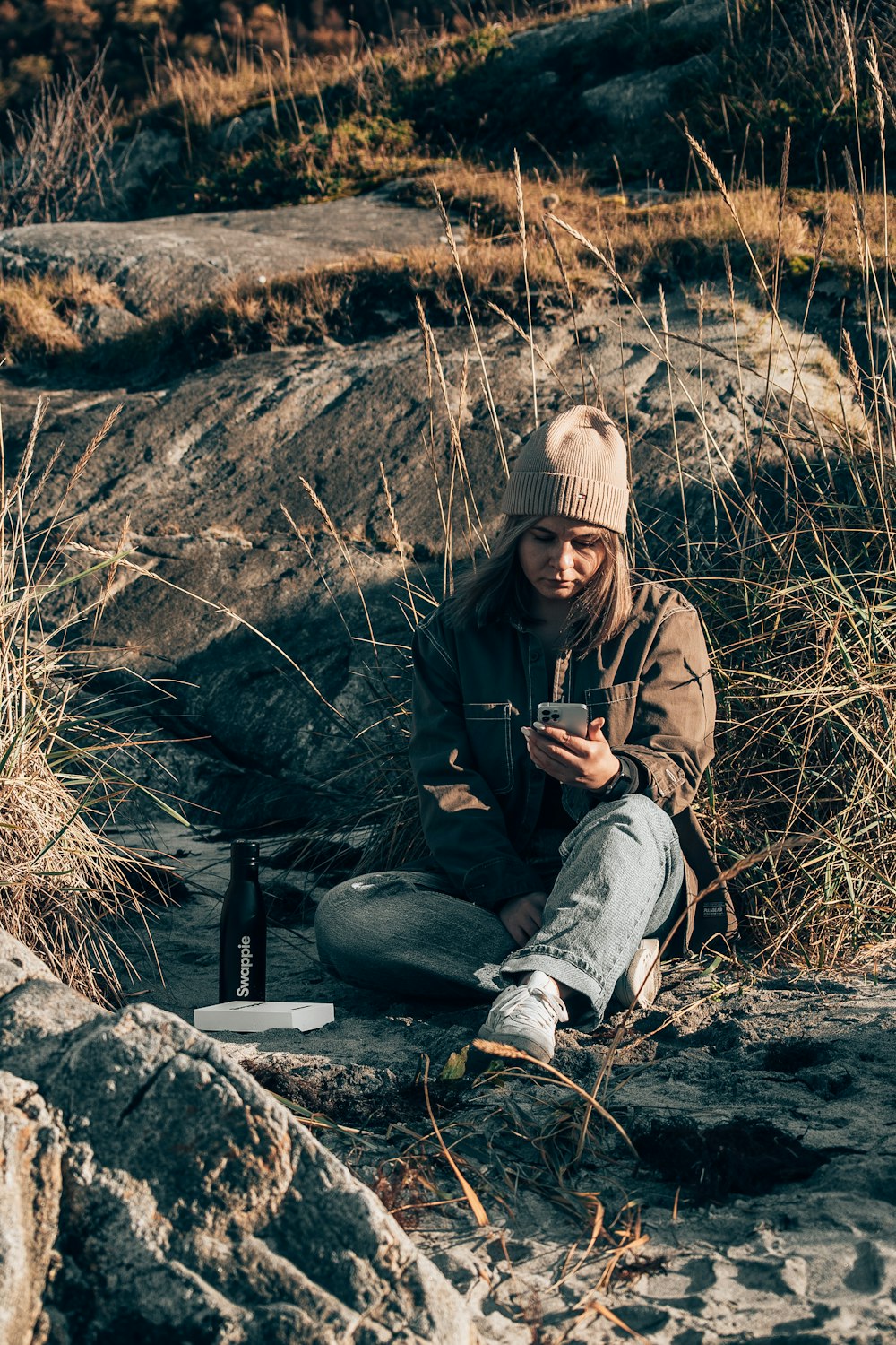 a person sitting on a rock looking at a cell phone