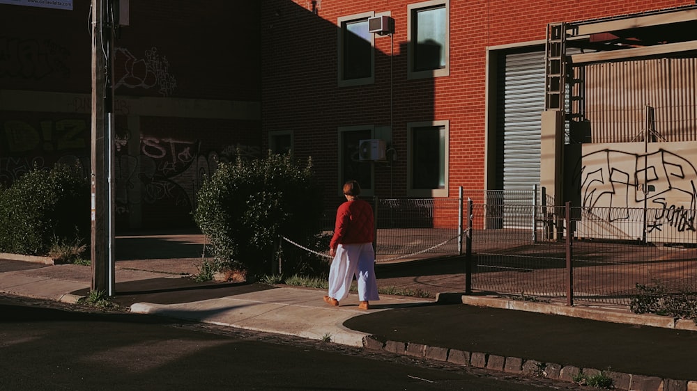 a woman walking down a street past a red brick building