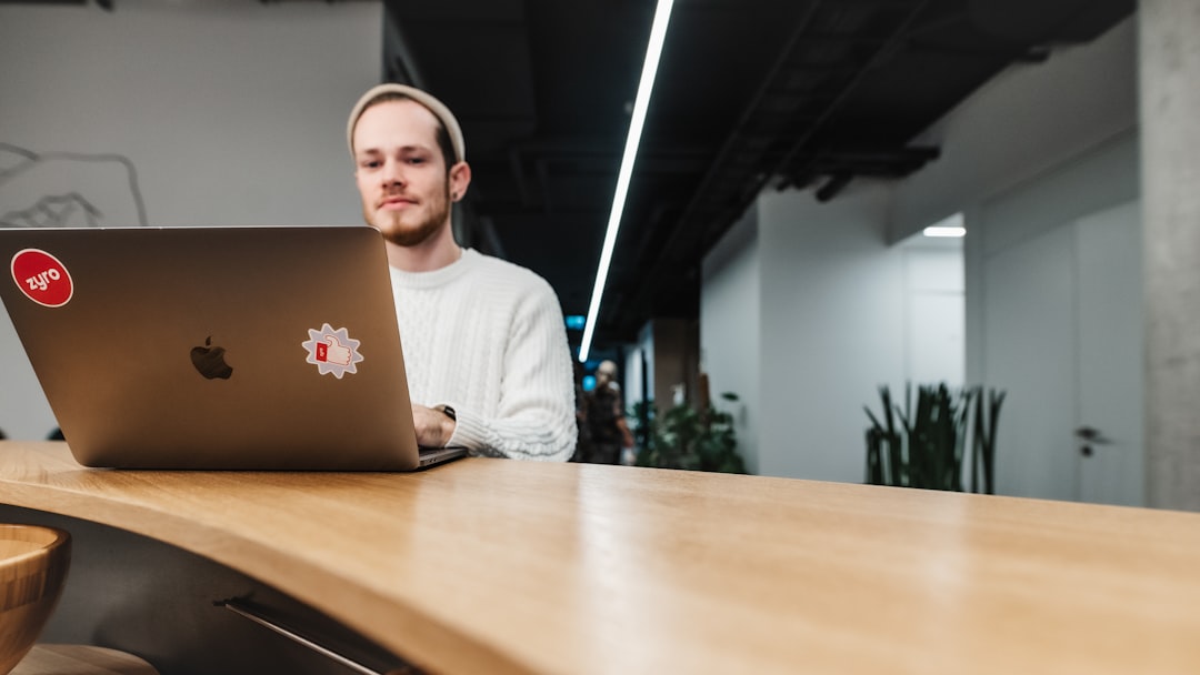 a man sitting in front of a laptop computer, A man working on his laptop computer in an office space
