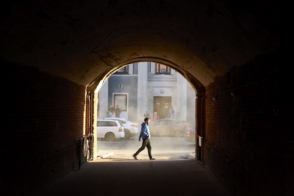 a man walking through a tunnel in the middle of a street