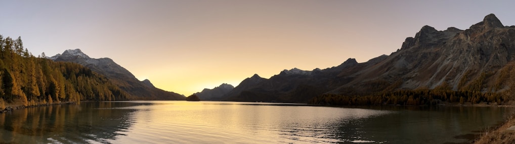 A serene lake surrounded by lush green mountains at sunset.