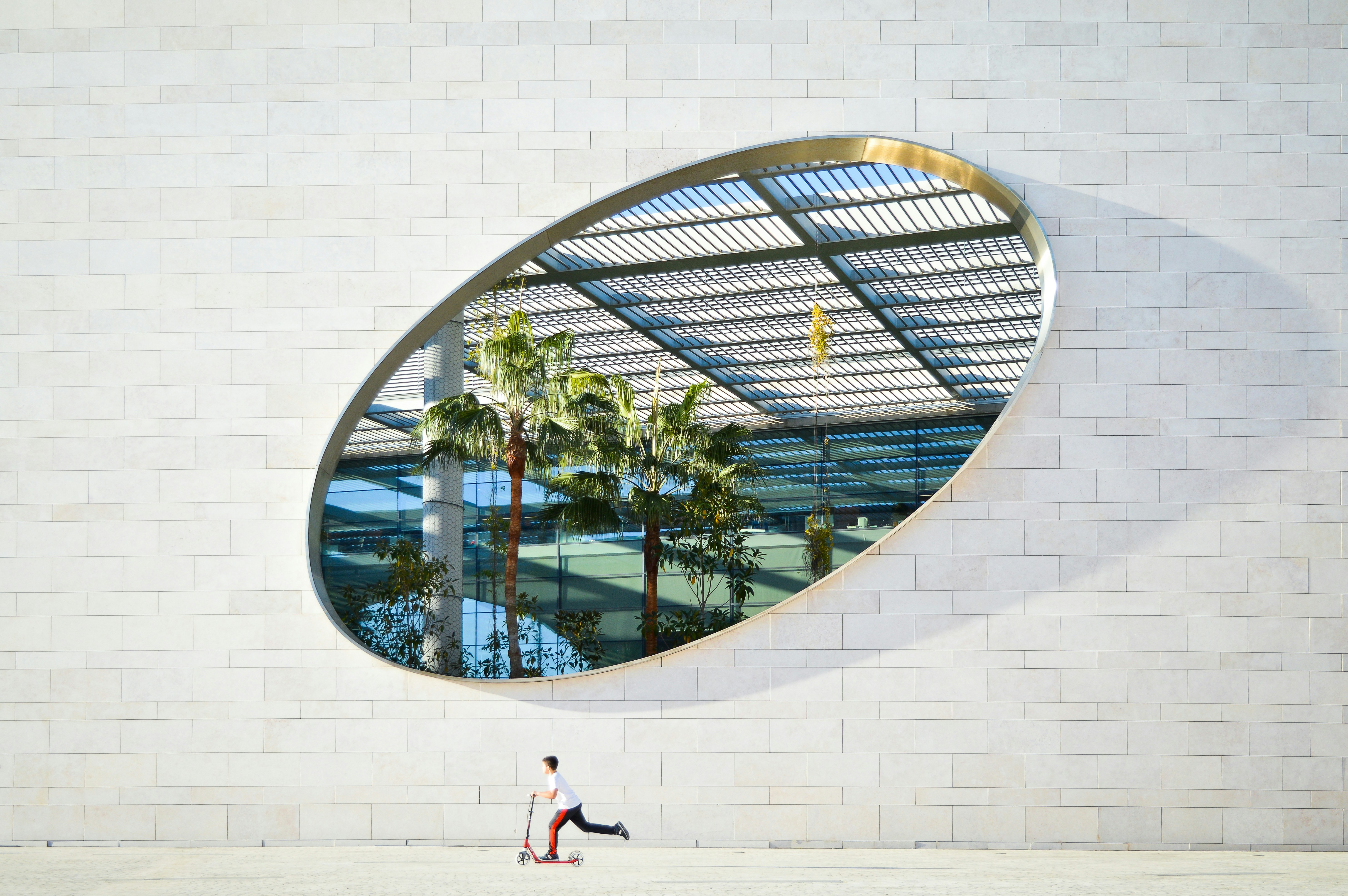 a person walking past a building with a large circular mirror on the wall