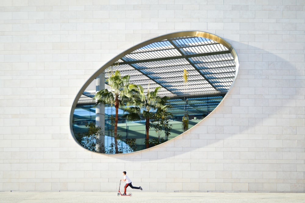 une personne passant devant un bâtiment avec un grand miroir circulaire sur le mur