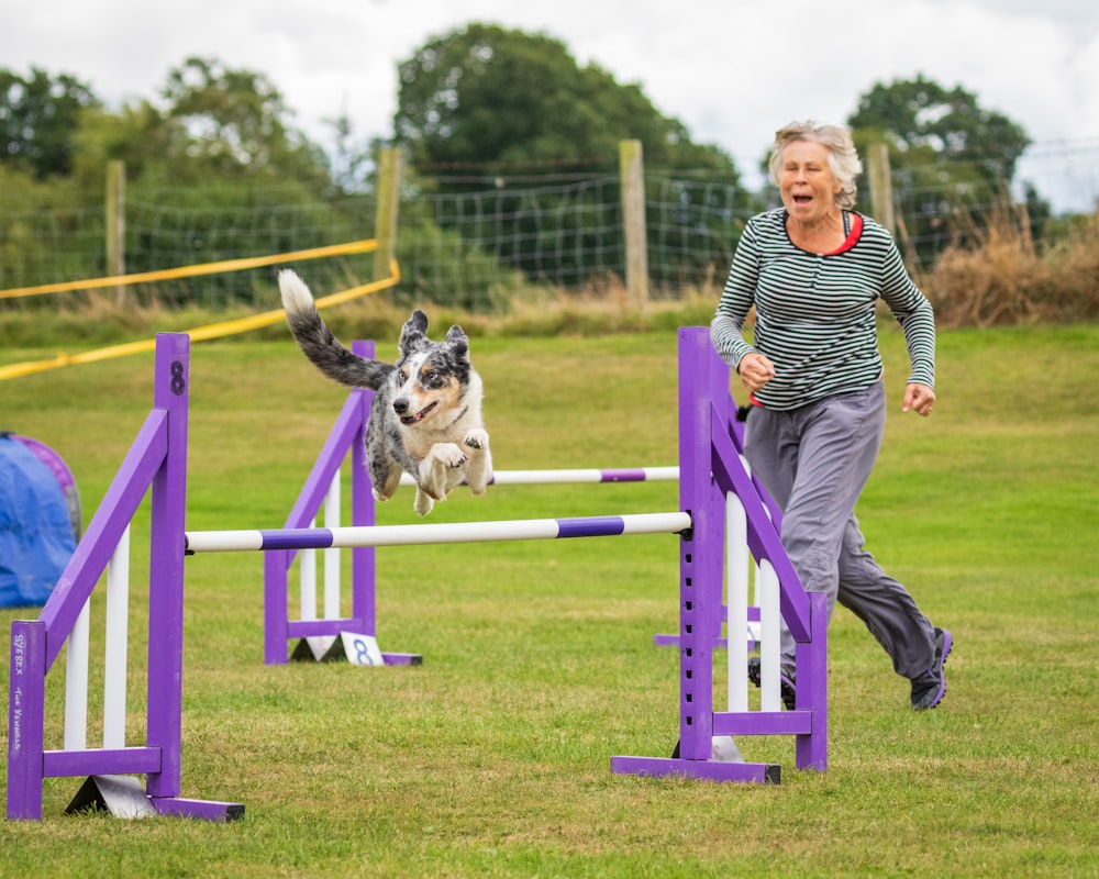 a woman and a dog running over a hurdle