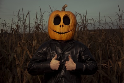 a man wearing a pumpkin mask standing in a corn field