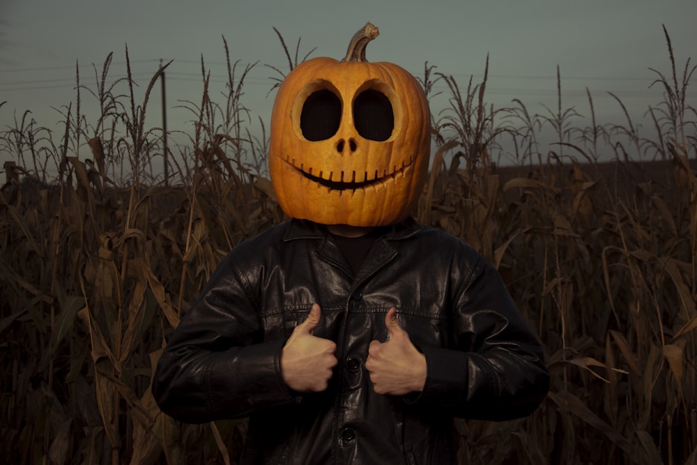 a man wearing a pumpkin mask standing in a corn field