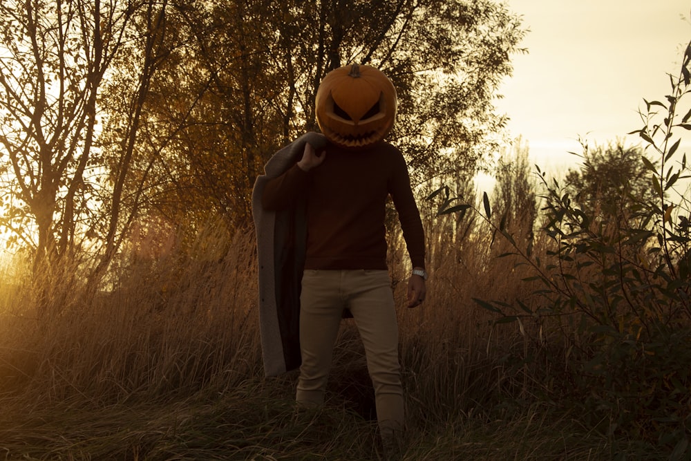 a man wearing a pumpkin hat walking through a field