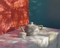 A ceramic teapot and cup sit on a marble surface. The scene is softly lit with natural light casting shadows of leaves and branches against a red and teal background, creating a tranquil atmosphere.