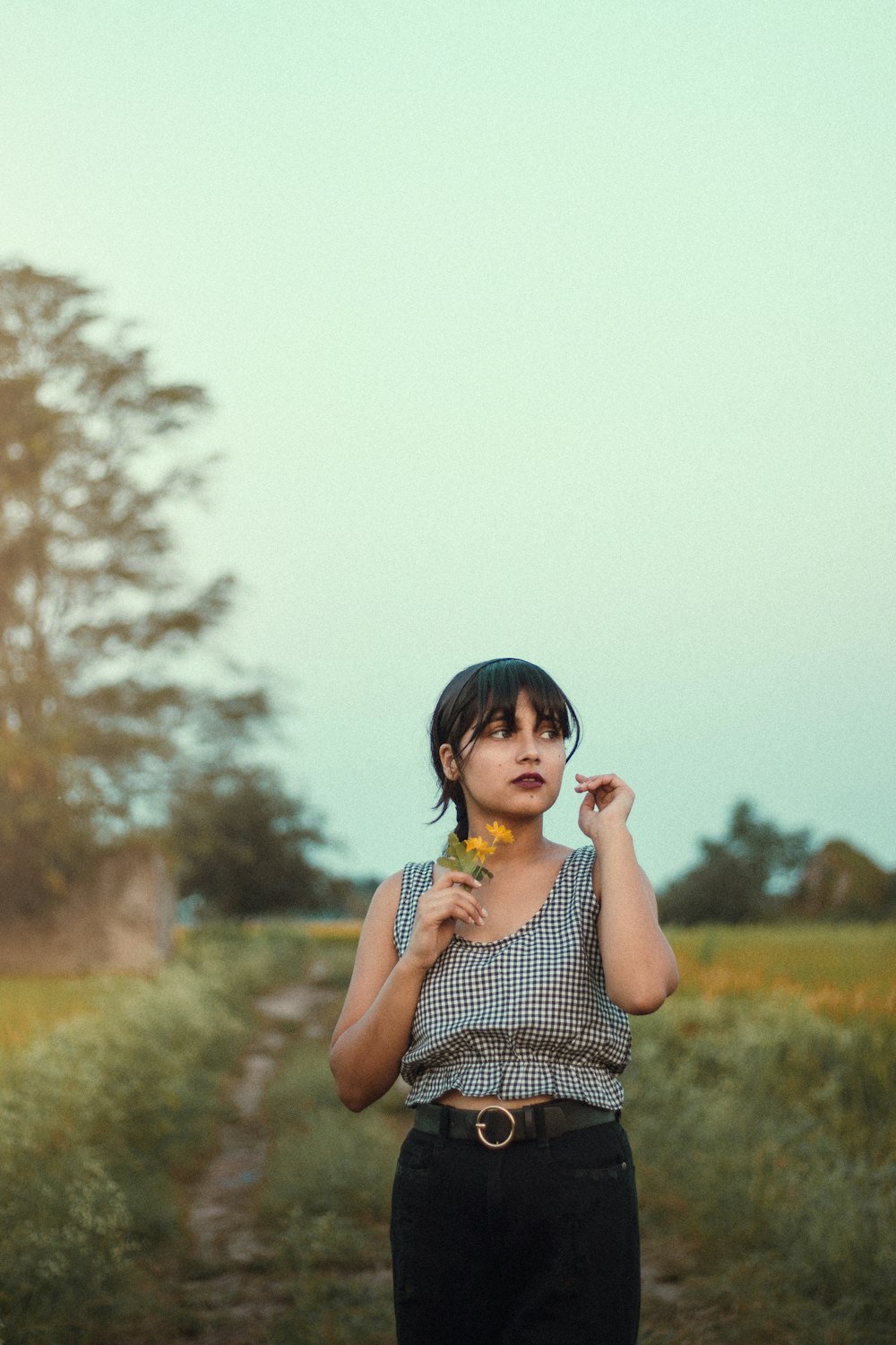 a woman standing on a dirt road holding a flower