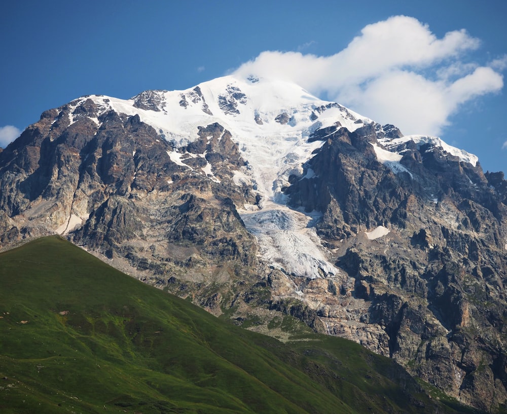 a large mountain covered in snow and green grass