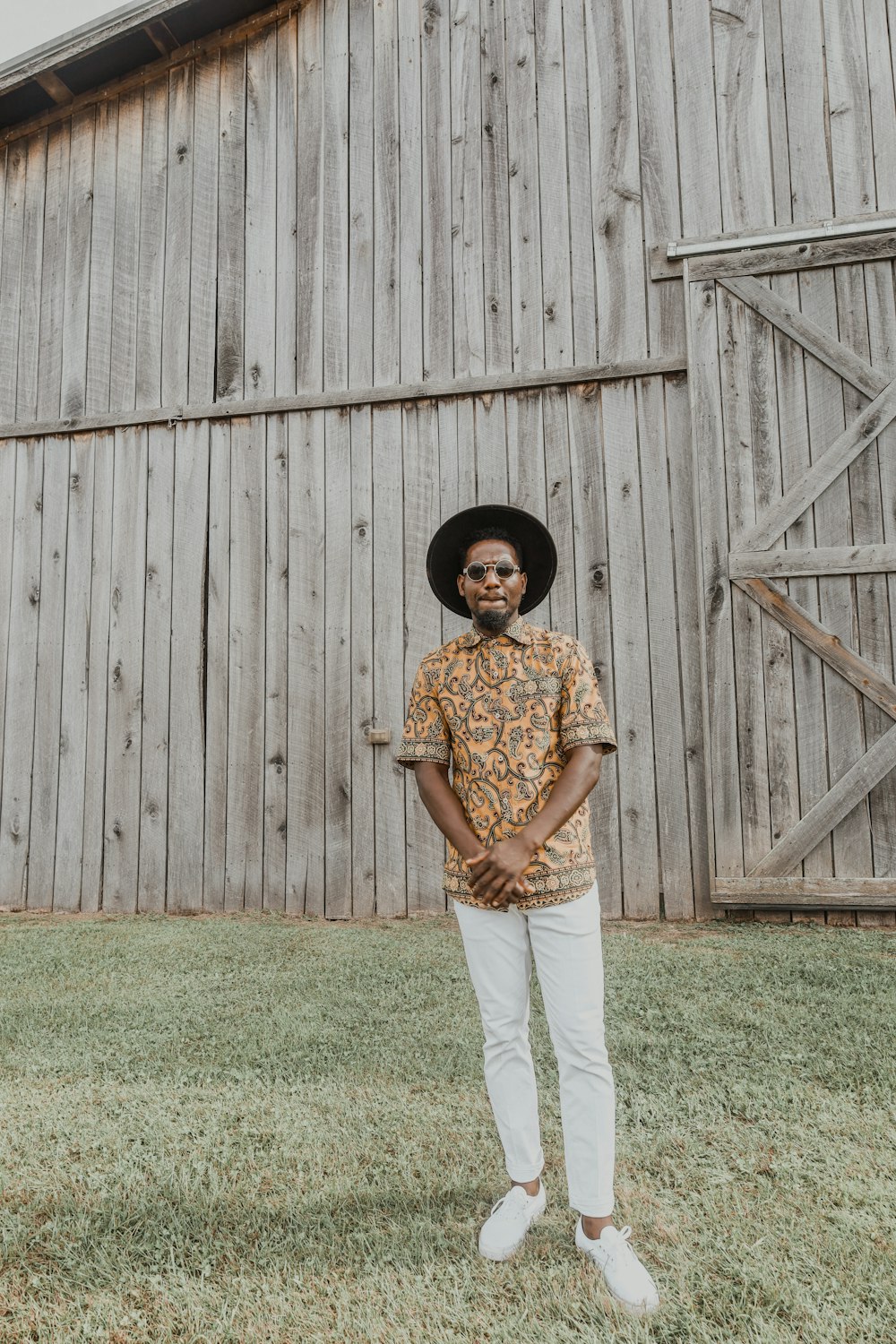 a man standing in front of a barn wearing a hat