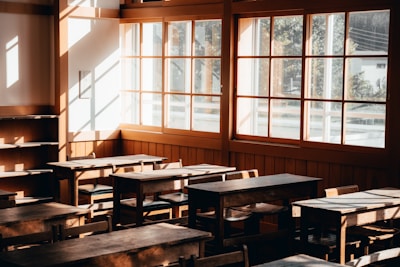 A cozy classroom with natural wooden furniture and sunlight streaming through large windows.
