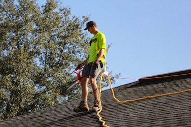 a man in a yellow shirt with a chainsaw on a roof