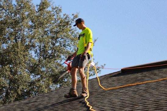 a man in a yellow shirt with a chainsaw on a roof